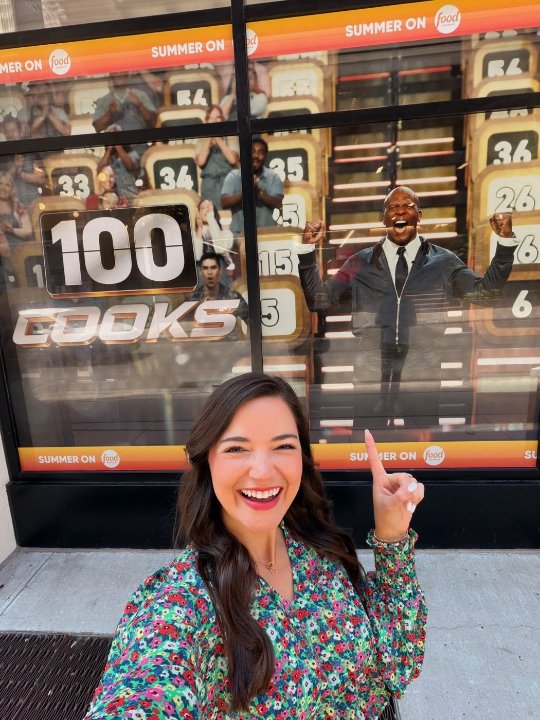 Holley pointing at the 100 Cooks billboard on Food Network